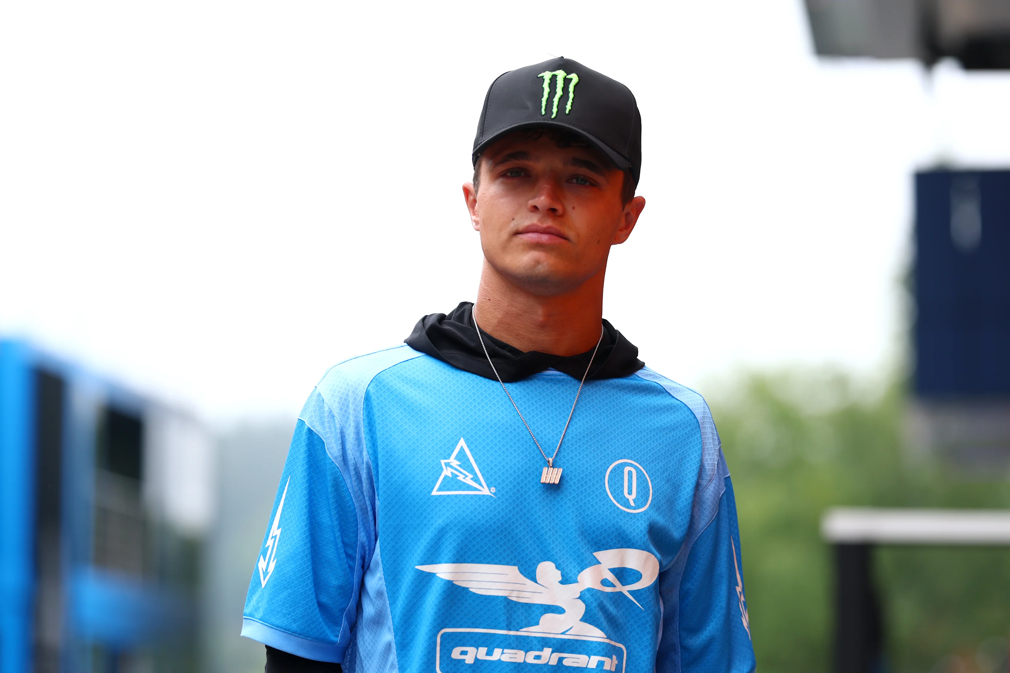 Lando marche sur le paddock avant le Grand Prix belge 2025 portant une chemise de style en jersey de son propre quadrant de marque. Swipe pour en voir plus